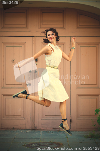 Image of woman in a white dress smiles and jumps near the old door