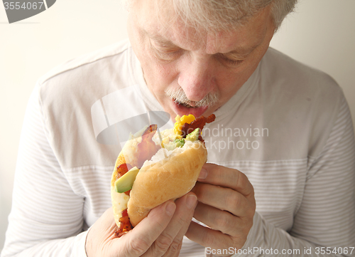 Image of Older man eats bacon, egg and avocado sandwich 