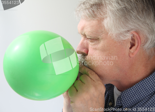 Image of senior man blowing up balloon