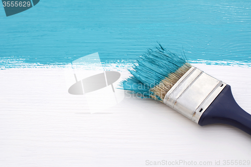 Image of Paintbrush with blue paint, painting over white board