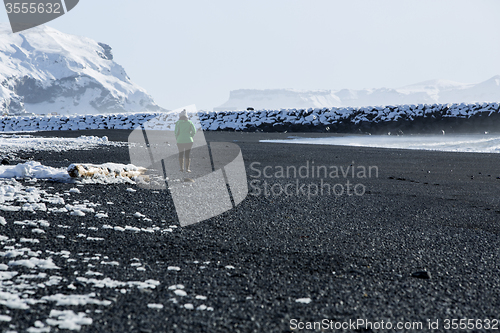 Image of Woman walks along black sand beach in Vik, Iceland