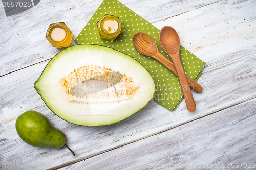 Image of Cut melon green pear and honey on rustic board