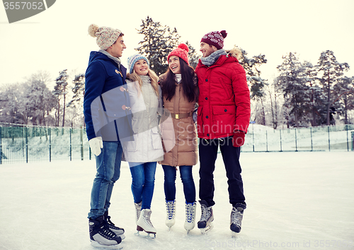 Image of happy friends ice skating on rink outdoors