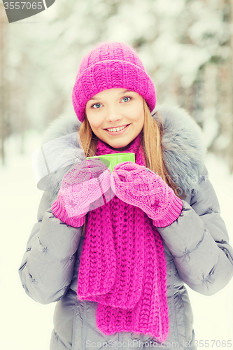 Image of smiling young woman with cup in winter forest