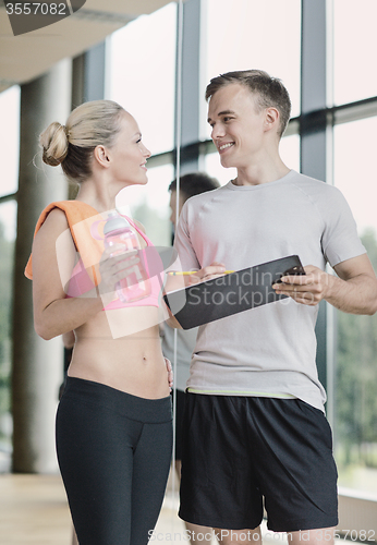 Image of smiling young woman with personal trainer in gym