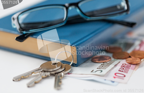 Image of close up of book, money, glasses and keys on table