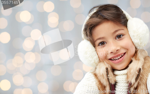 Image of happy little girl in earmuffs over holidays lights