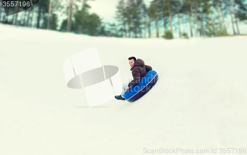 Image of happy young man sliding down on snow tube