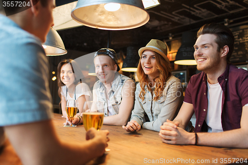 Image of happy friends drinking beer and talking at bar