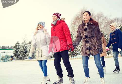 Image of happy friends ice skating on rink outdoors