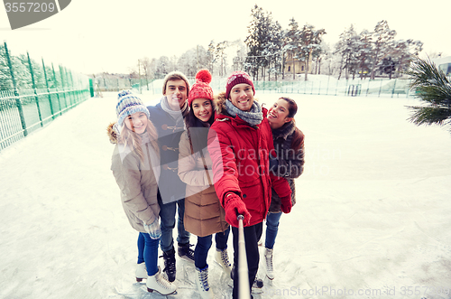 Image of happy friends with smartphone on ice skating rink