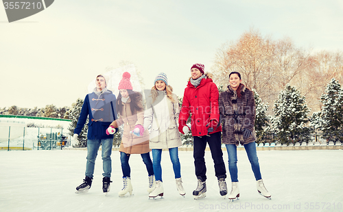 Image of happy friends ice skating on rink outdoors