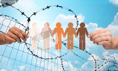 Image of hands holding people pictogram over barb wire