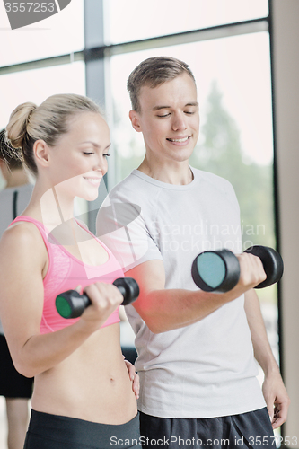 Image of smiling young woman with personal trainer in gym