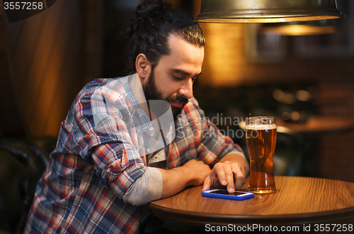 Image of man with smartphone and beer texting at bar