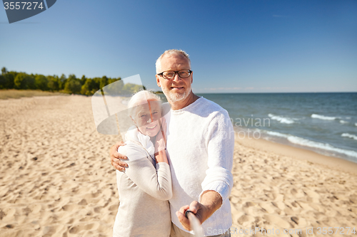 Image of seniors taking picture with selfie stick on beach