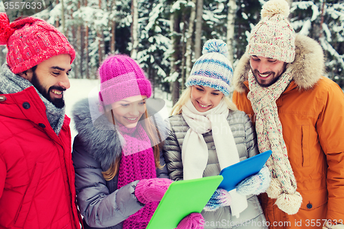 Image of smiling friends with tablet pc in winter forest