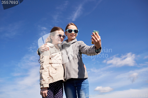 Image of happy girls with smartphone taking selfie outdoors
