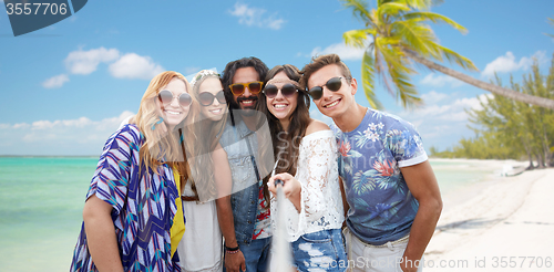 Image of happy hippie friends with selfie stick on beach