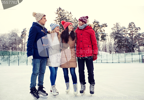 Image of happy friends ice skating on rink outdoors