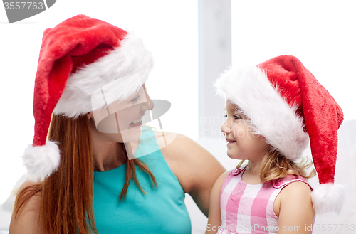 Image of happy mother and little girl in santa hats at home