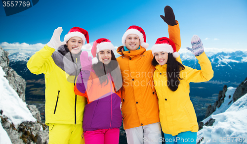 Image of happy friends in santa hats and ski suits outdoors