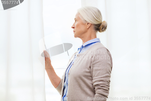 Image of lonely senior woman looking through window at home