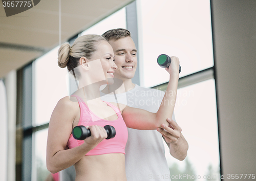 Image of smiling young woman with personal trainer in gym