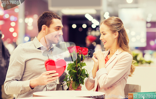 Image of happy couple with present and flowers in mall