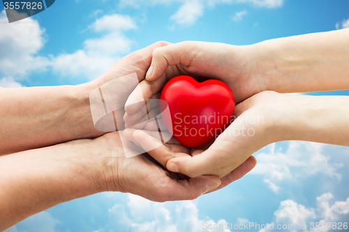 Image of senior and young woman hands holding red heart