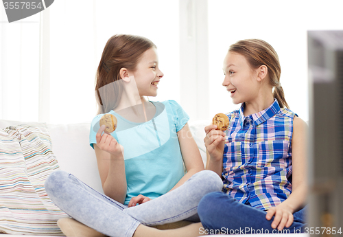 Image of happy girls watching tv and eating cookies at home