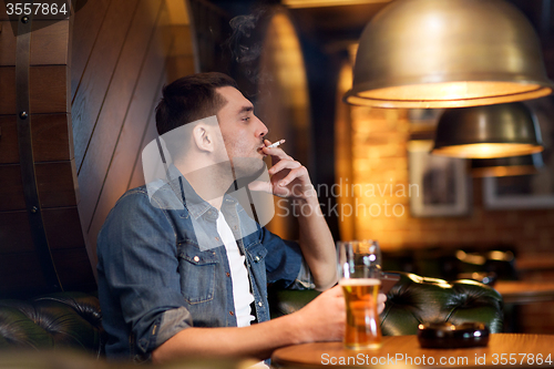 Image of man drinking beer and smoking cigarette at bar