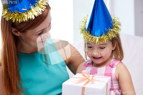 Image of happy mother and child in party caps with gift box