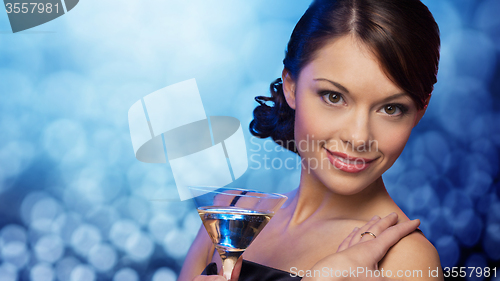 Image of smiling woman holding cocktail over blue lights