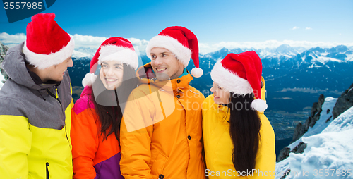 Image of happy friends in santa hats and ski suits outdoors