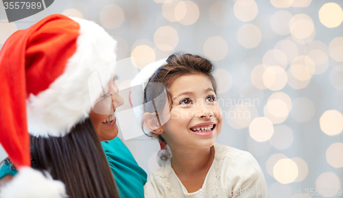 Image of happy mother and little girl in santa hats at home