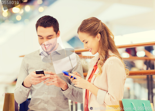 Image of couple with smartphones and shopping bags in mall