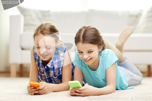 Image of happy girls with smartphones lying on floor