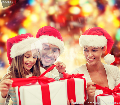 Image of happy family in santa hats sitting with gift boxes