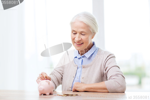 Image of senior woman putting money to piggy bank at home