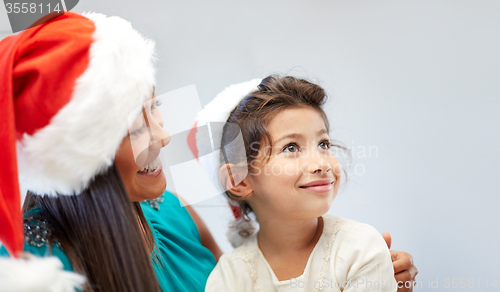 Image of happy mother and little girl in santa hats at home