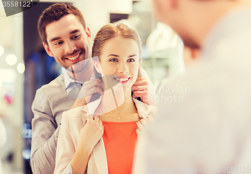 Image of couple trying golden pendant on at jewelry store