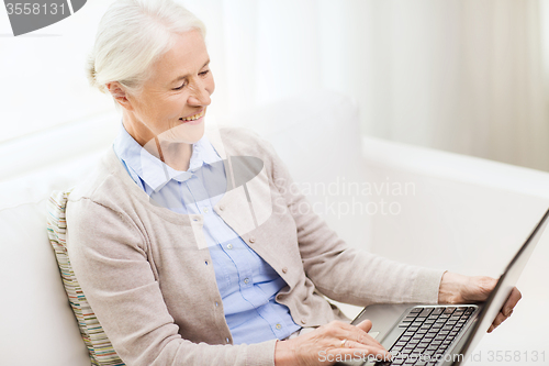 Image of happy senior woman with laptop at home