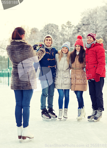 Image of happy friends with smartphone on ice skating rink