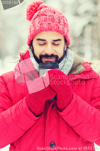 Image of smiling young man with cup in winter forest