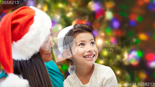 Image of happy mother and little girl in santa hats at home