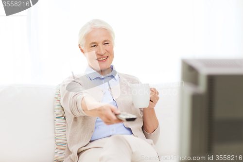 Image of senior woman watching tv and drinking tea at home