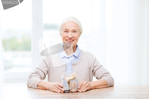 Image of senior woman with money in glass jar at home