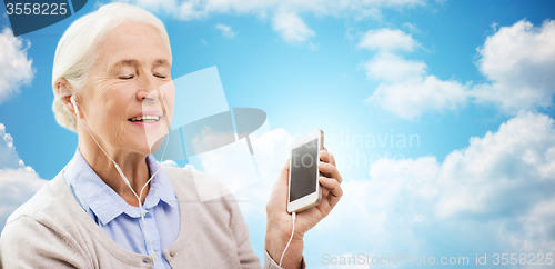 Image of senior woman with smartphone and earphones at home