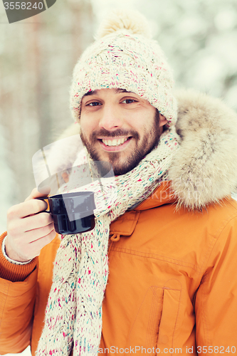 Image of smiling young man with cup in winter forest